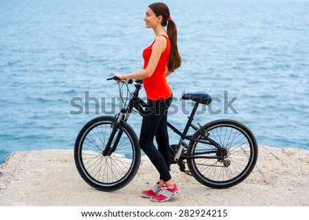 Sport woman in red shirt standing with bicycles on the concrete seacoast
