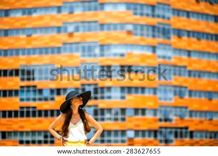 Young woman in black hat standing on the contemporary colorful facade background. General plan with space for your text
