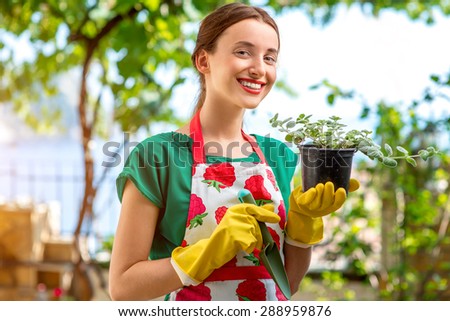 Young woman in apron and working gloves taking care for  flower in in the garden