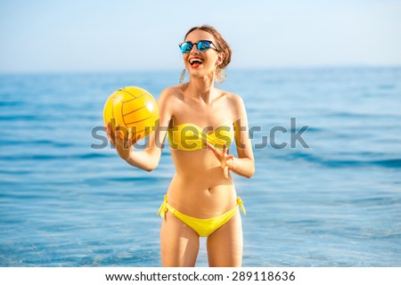 Young playful woman standing in the water with yellow ball on the beach. Summer water game concept