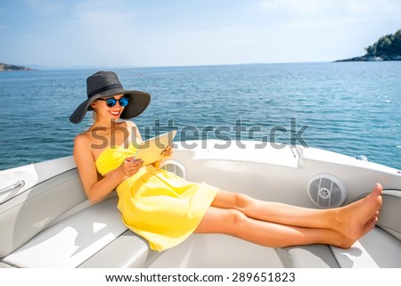 Young woman in yellow swimsuit and skirt reading with digital tablet on the yacht floating in the sea