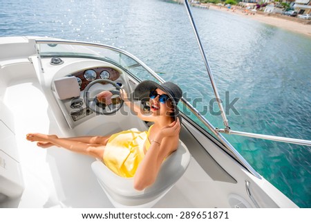Young and pretty woman in yellow skirt and swimsuit with hat and sunglasses driving luxury yacht in the sea. Top view with copy space