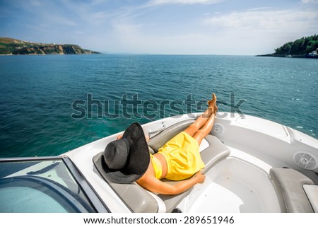 Young and pretty woman in yellow swimsuit with big hat relaxing on the yacht floating in the sea. Luxury summer recreation