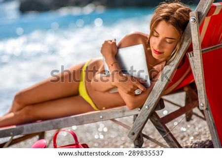 Young and pretty woman hugging with digital tablet on the red sunbed on the beach