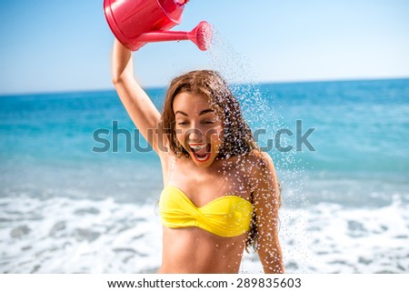 Emotional woman pouring water from watering can on the beach. Summer positive emotions
