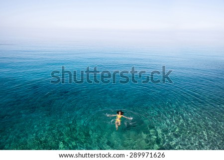Young woman in yellow swimsuit swimming and relaxing in the blue water sea. Top view, general plan with copy space