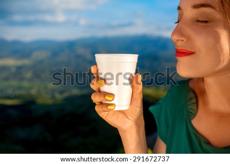 Young woman holding white coffee paper cup on the mountain background. Take away coffee concept