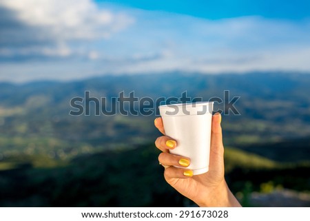 Holding white paper coffee cup outdoors on mountain backgraound. Take away coffee concept