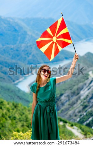 Young happy woman in green dress holding macedonian flag on the top of mountain near Kozjak lake in Macedonia. Promoting tourism in Macedonia