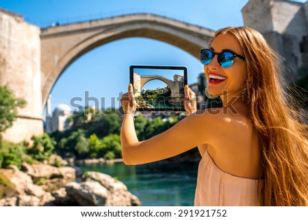 Female tourist photographing with digital tablet old bridge in Mostar city in Bosnia and Herzegovina.