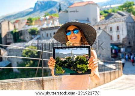 Woman showing tablet with photo of Mostar city standing on the old bridge. Promoting tourism in Bosnia and Herzegovina