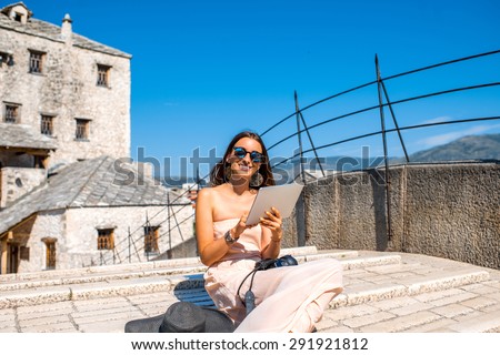 Female tourist using digital tablet sitting on the old bridge in Mostar city in Bosnia and Herzegovina