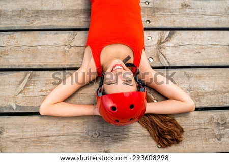 Young woman in red shirt and helmet resting on the wooden pier. Close up, top view