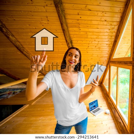 Young and cute woman designing or projecting a house with digital tablet standing near the window in cozy wooden cottage.
