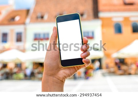 Female hands holding smart phone with white screen on old city background. Travel program concept