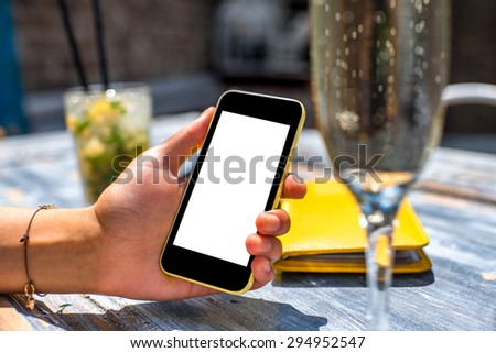 Female hand using a phone with isolated screen on wooden vintage table holding a glass with mohito