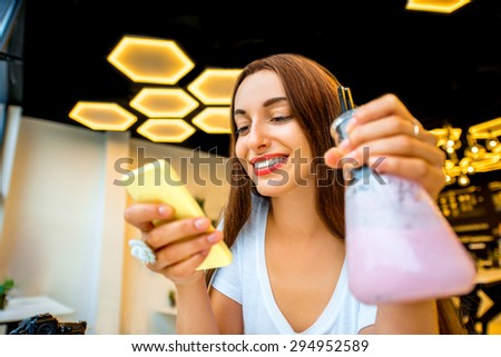 Young woman using phone and holding beaker with drink in modern interior lab or cafe