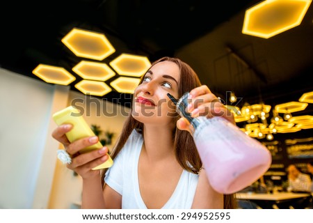 Young woman using phone and holding beaker with drink in modern interior lab or cafe