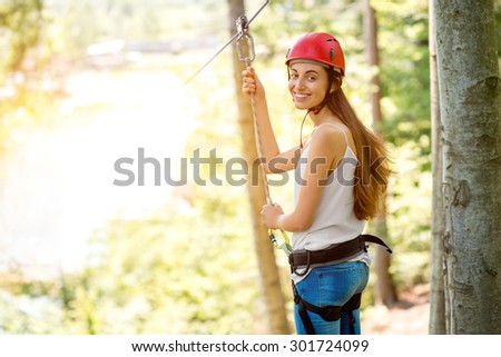 Young and smiling woman in red helmet preparing to ride on a zip line in the forest. Close up view focused on hands and face
