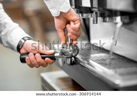 Barista pressing coffee in the coffee machine holder. Close up view focused on hands
