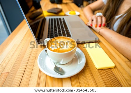 Aroma cappuccino with flower shape with phone and laptop on the wooden table