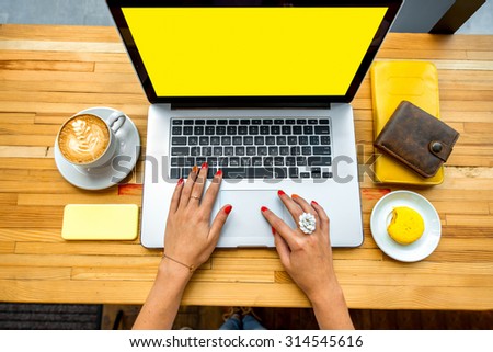 Female hands typing on the laptop with coffee cup, phone, sweet cake and wallet on the wooden table