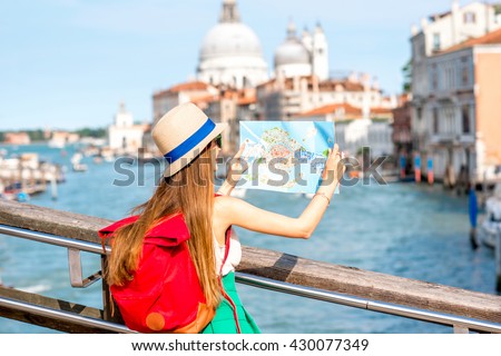 Young female traveler with hat and backpack traveling with paper map on the bridge with great view on Grand canal in Venice.