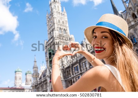 Young female tourist making heart shape with hands on the town hall building background in Munich. Having a great vacation in Germany