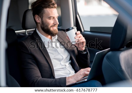 Handsome businessman sitting with coffee to go on the backseat of the car