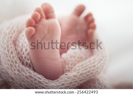 Soft newborn baby feet against a pink blanket.