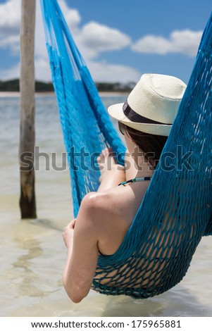 Woman relaxing on hammock with white hat sunbathing on vacation at Jericoacoara, Brazil