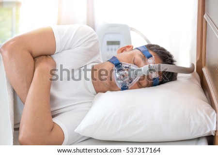 Sleep apnea therapy,Man sleeping in bed wearing CPAP mask. \
Happy and healthy senior man sleeping deeply on his left side without snoring