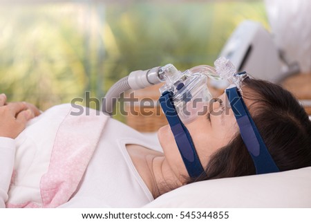 Sleep apnea therapy, Woman sleeping in bed wearing CPAP mask.\
Happy and healthy senior woman sleeping deeply on her back quietly without snoring,blurred CPAP machine background