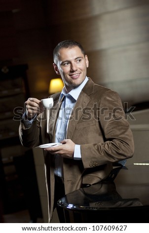 Man dressed on suite drinks cup of coffee inside hotel lobby.