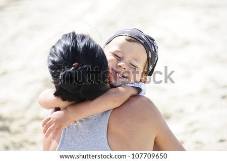 Small boy is hugging his mom on the beach.