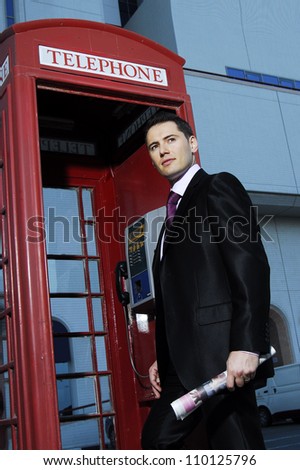 Successful yang man in business suit posing in front of vintage phone booth.