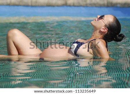 Yang and beautiful pregnant woman lying down in shallow clean sea water.