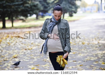 Yang and cute pregnant woman walks alone on Autumn background
