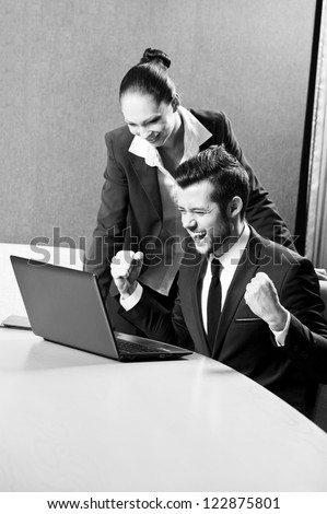 Two business persons posing in office with lap top.