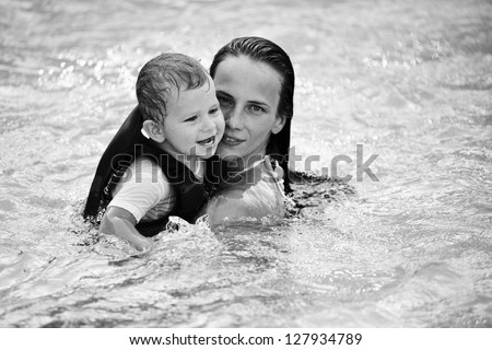 Beautiful young mom plays in the pool with her baby son.