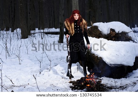 Portrait of red haired beautiful and wild yang woman the hunter in the winter gloomy forest.