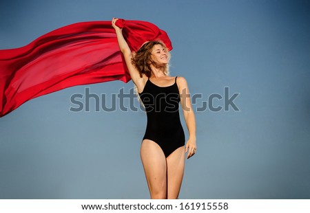 Professional gymnast woman dancer posing in front of sunset sky and red fabric background