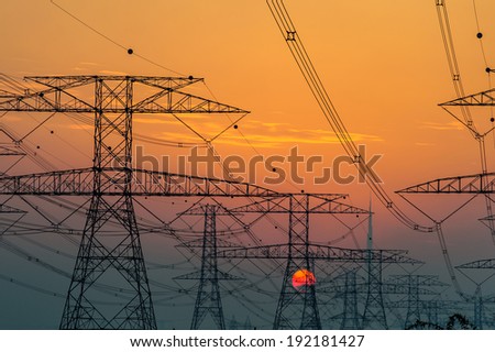 High voltage power lines with electricity pylons at twilight. At the horizon of sunset sky in Dubai desert.