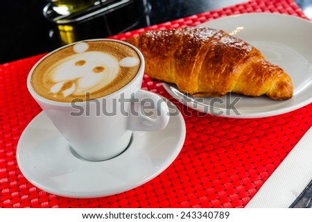 Cappuccino in a cup with croissant in table.