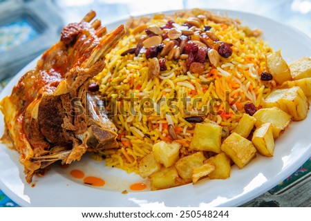Plate of yellow rice topped with mutton meat and potatoes.