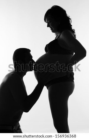 Husband kissing the wife\'s belly in silhouette Loving father kissing the belly of his pregnant wife  in silhouette
