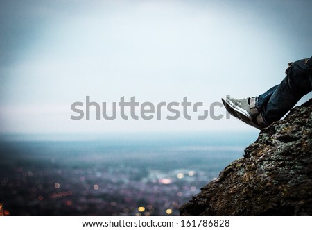 The young man sits on a rock above the city in the sunset