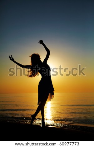 Girl dances on the beach at sunset. Natural light and dark. Artistic colors added. Vertical photo