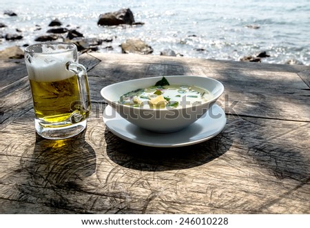 A glass of beer and a bowl with green curry chicken soup on a table by the ocean on Koh Chang