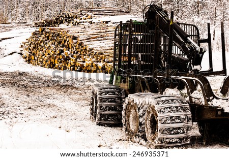 Forestry tractor in front of piles with lumber in winter landscape,